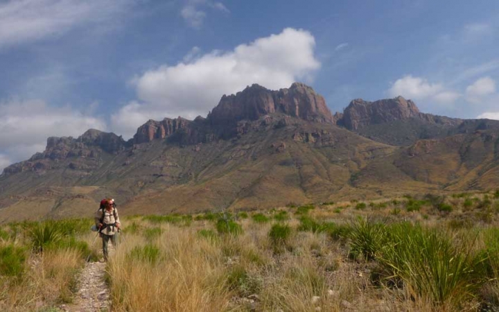 an outward bound student carrying a backpack stands on a desert trail with a rocky mesa in the background